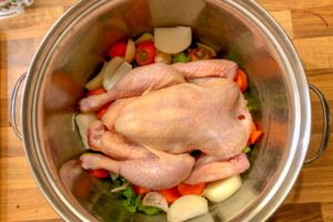 a whole chicken in a big pot on top of chopped root vegetables ready to make a stock