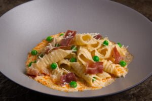 garganelli pasta in a bowl with peas, parma ham, and a cream sauce.