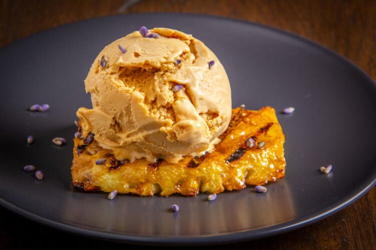 a scoop of caramel ice cream on top of a slice of grilled pineapple with a garnish of lavender pieces