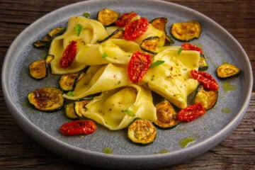 tortelloni salad on a grey plate dressed with a balsamic vinaigrette with oven dried tomatoes, small slices of fried zucchini and fresh basil